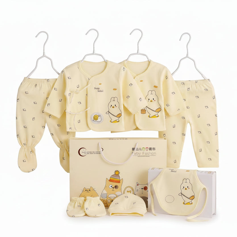 A baby clothing set displayed on white hangers with a matching gift box, bib, and booties. The set includes a long-sleeve top, matching pants, a bib, a hat, and booties, all in a soft pale yellow color with small cartoon bunny prints.